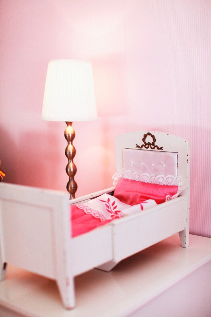 Old dolls' bed with lace bed covers and lamp with brass base on bedside table