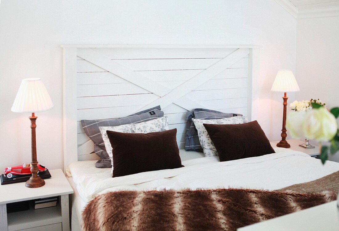 Double bed with half-height headboard made from wooden boards flanked by simple, Shaker-style lamps