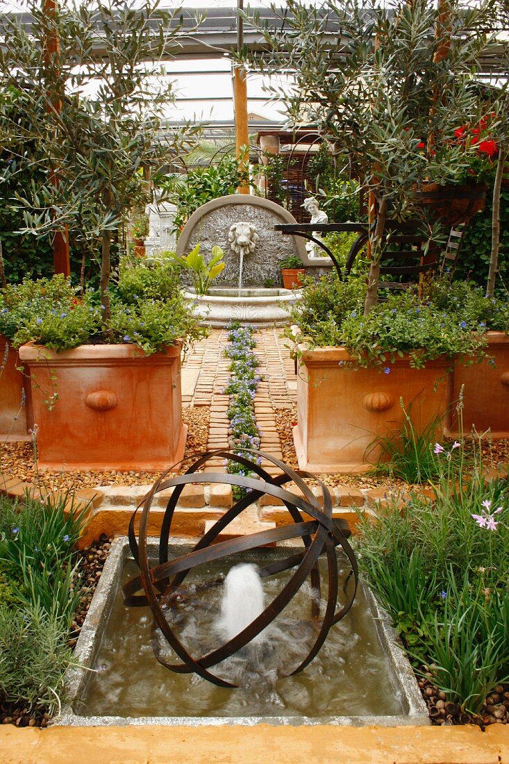 Mediterranean garden with terracotta pots and stylised stream of blue lobelia in paved floor between fountain and pool