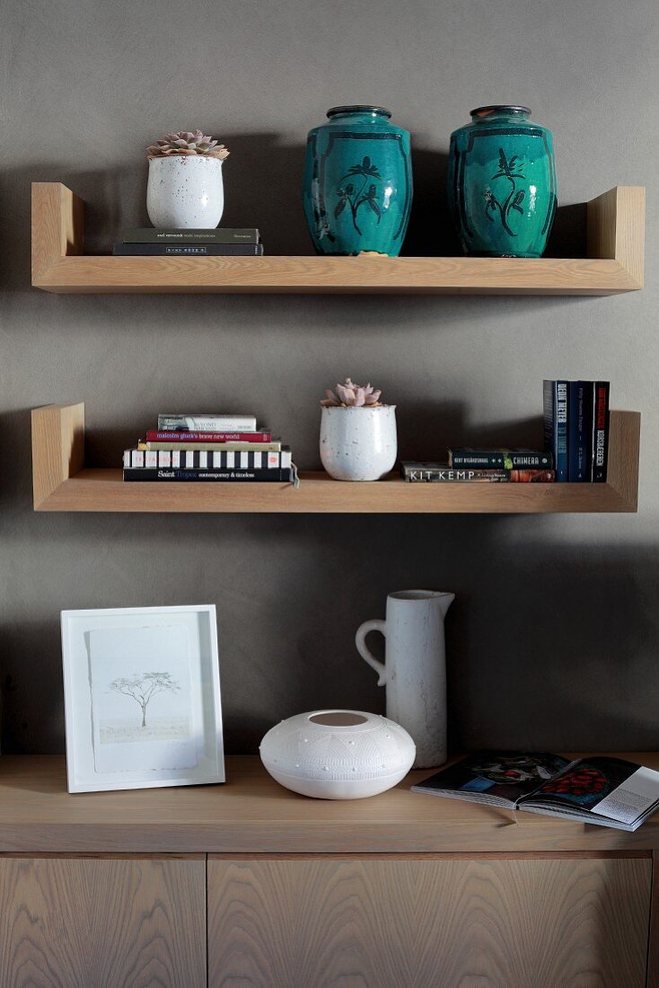 Turquoise ceramic vases on wooden shelves above sideboard against grey-painted wall