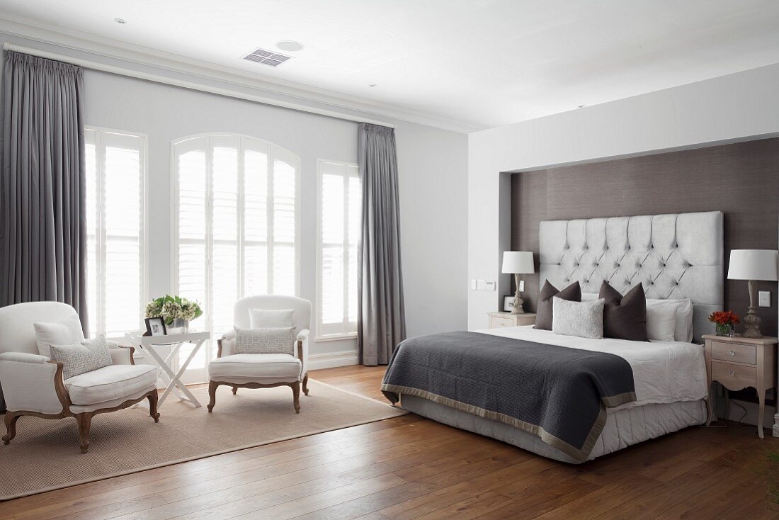 Schlafzimmer mit elegantem Doppelbett in Nische eines Raumteilers, gegenüber Salonecke mit Rokoko-Sesseln vor Fenster