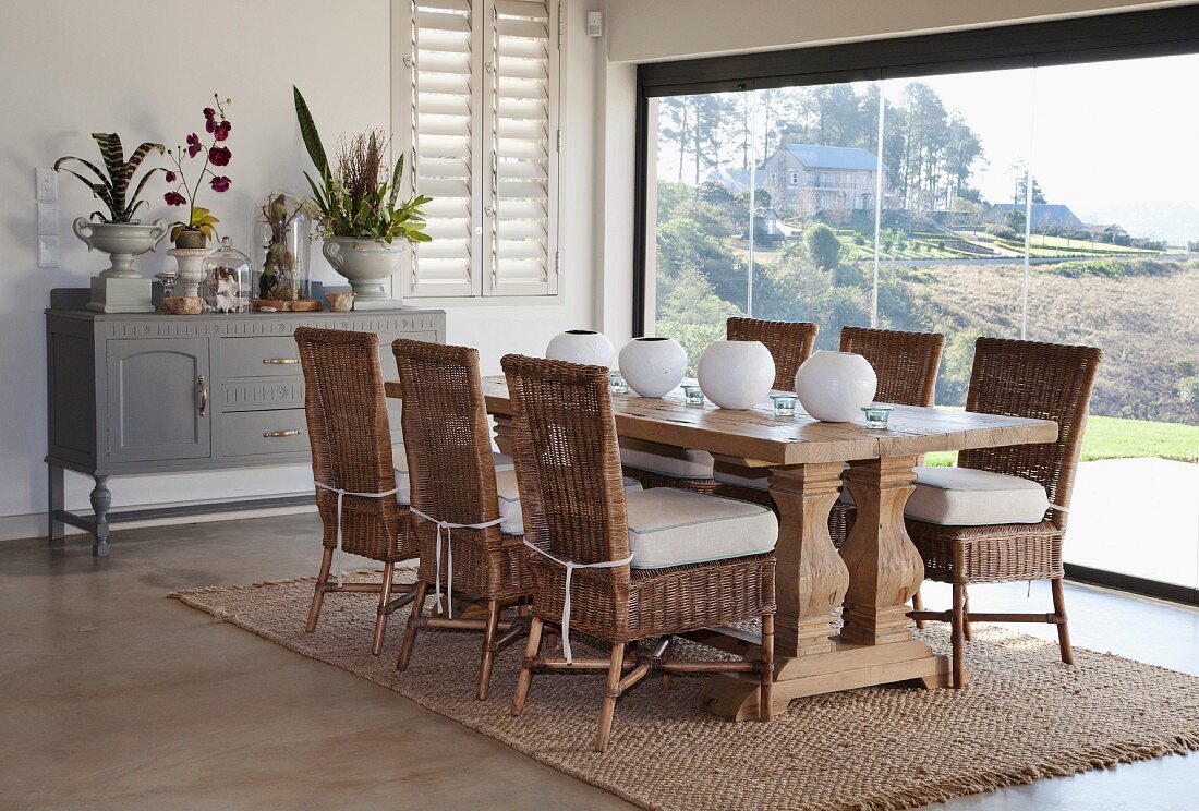 Dining area with wicker chairs, solid wooden table, spherical vases and panoramic window