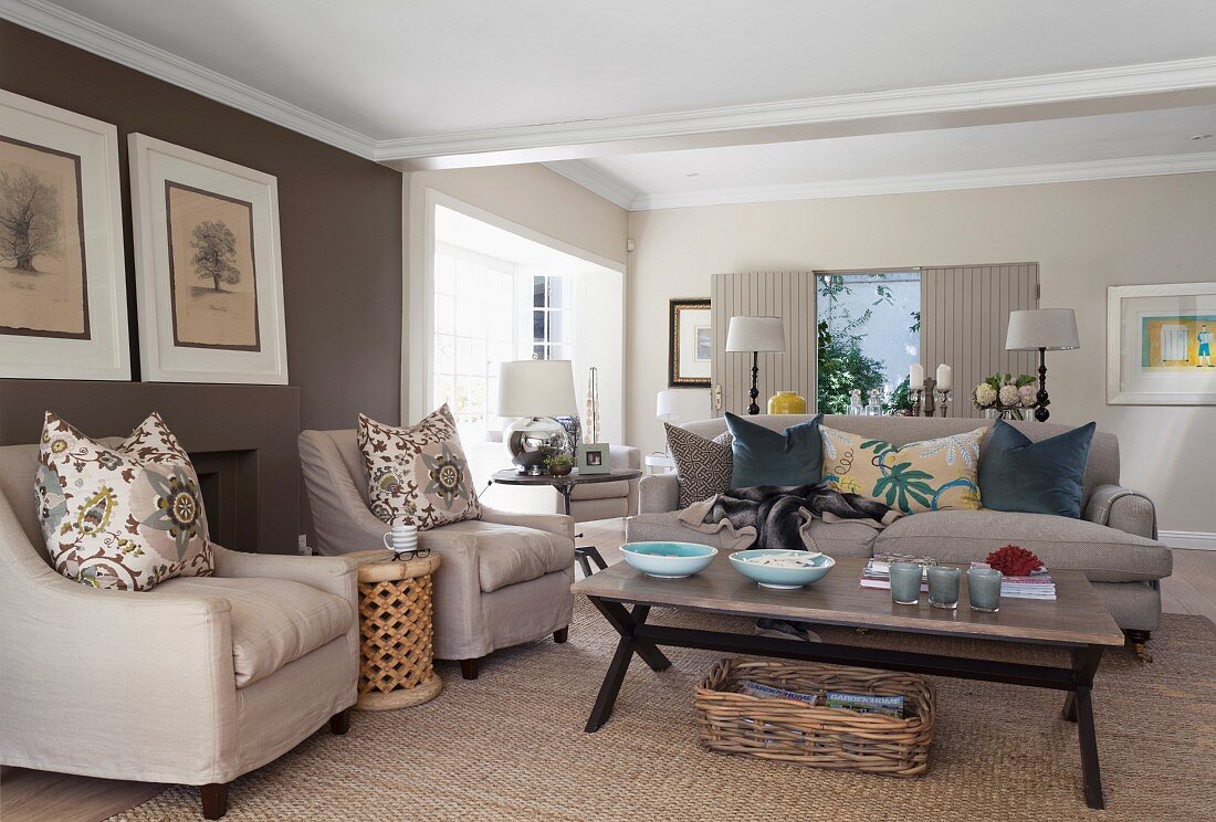 Pale armchairs with scatter cushions around coffee table in spacious living room with brown-painted accent wall