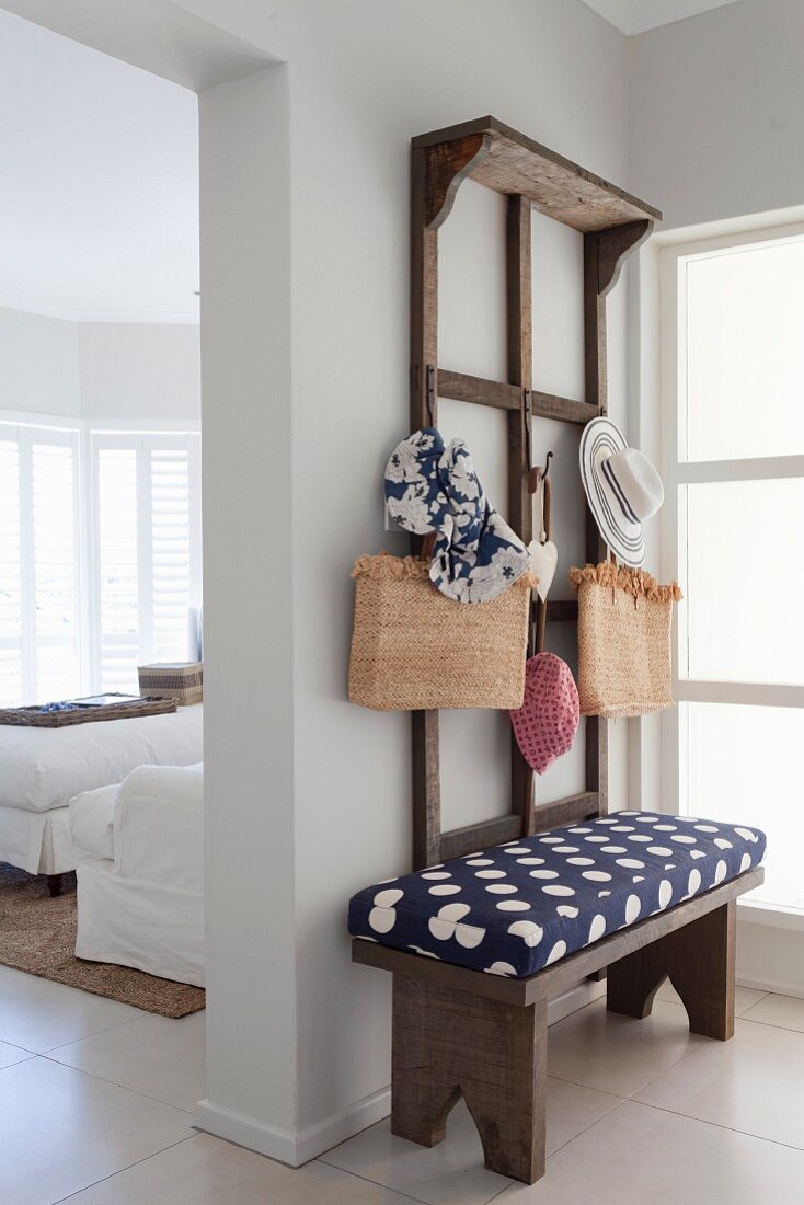 Wooden cloakroom bench with blue and white patterned cushions below accessories hung on wooden, wall-mounted rack