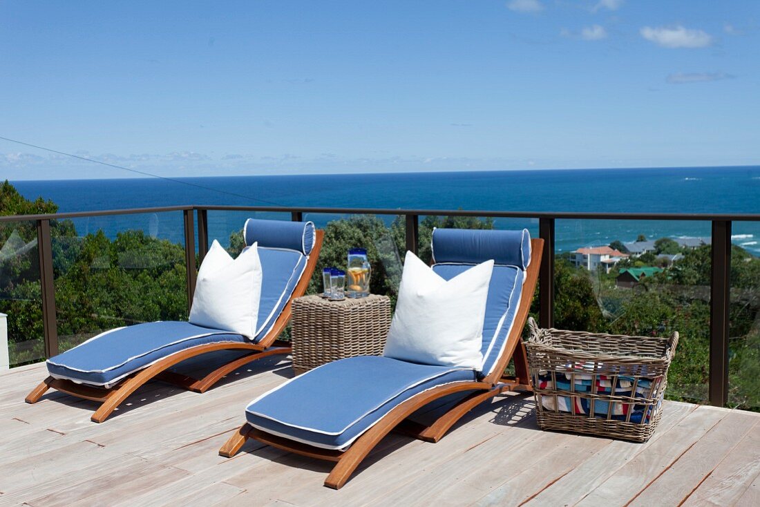 Sun loungers with blue mattresses and white pillows on wooden terrace with panoramic view of sea