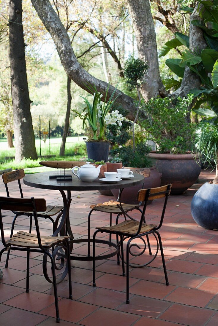 Gartenstühle und verschnörkeltes Tischgestell auf einer Terrasse unter Bäumen