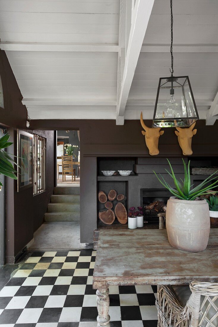 Wooden table in front of fireplace below stylised hunting trophies in dining room with chequered floor tiles
