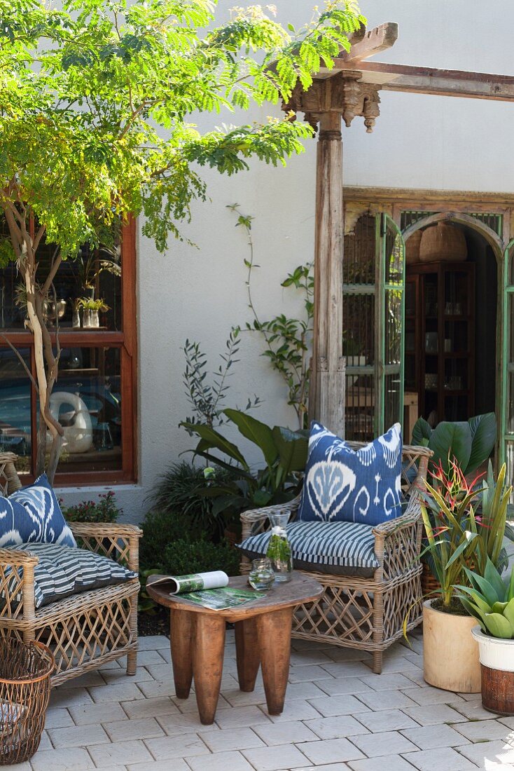 Wicker armchairs with batik cushions, African side table and potted plants on terrace