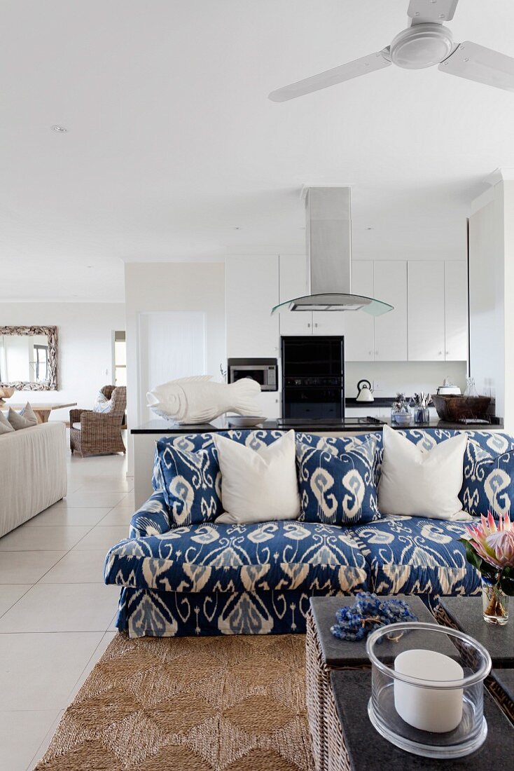 Sofa blau-weiss gemustert und teilweise sichtbarer Couchtisch in offenem Wohnraum, mit Küche im Hintergrund