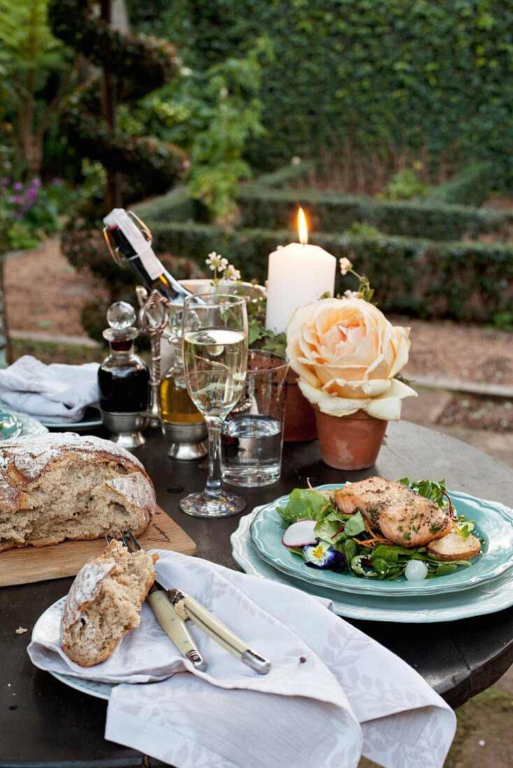 Salat mit Lachs und Brot auf Gartentisch mit festlichem Tischdeko