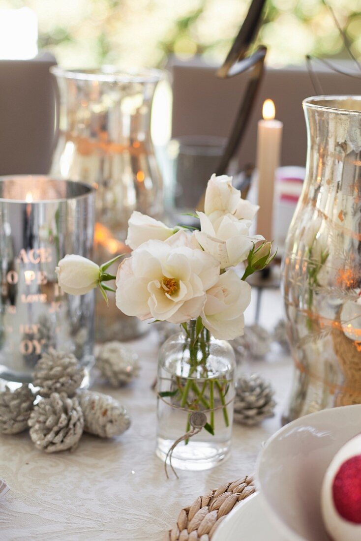 weiße Rosen im Glas zwischen silberfarbenen Windlichtern und weihnachtlicher Dekoration