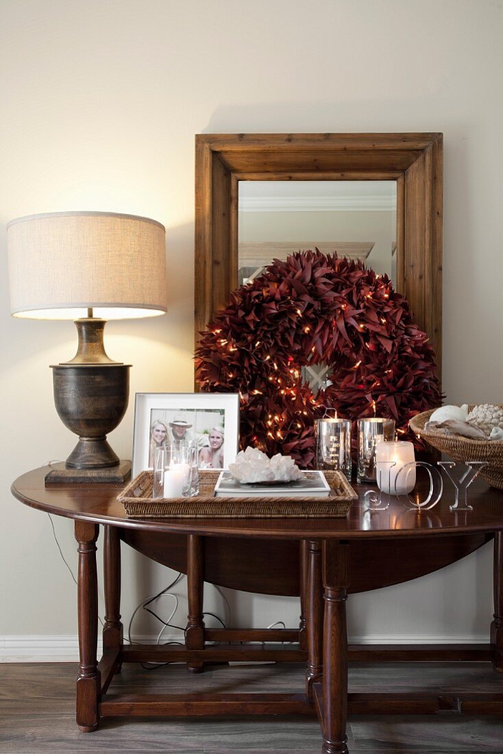 Dekorierter Holz Wandtisch mit weihnachtlichem Kranz aus roten Blättern und Windlichter, seitlich Tischleuchte mit hellem Stoffschirm