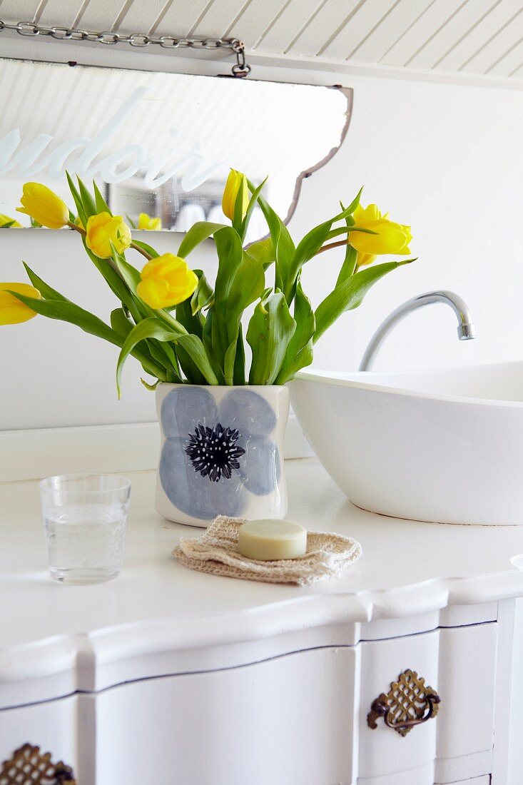 Vase of yellow tulips next to countertop basin on white washstand