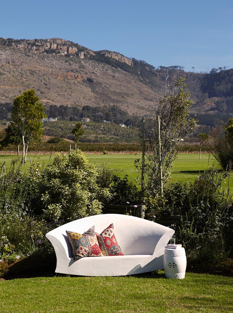 Outdoor Sofa in Weiß mit folkloristischen Kissen im Garten, im Hintergrund Berglandschaft