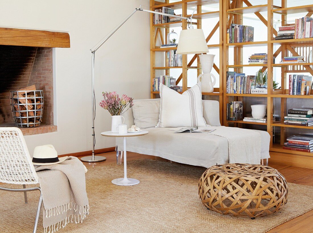 Wicker pouffe and chaise longue next to wooden partition shelving