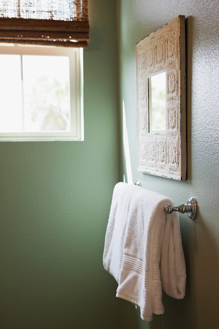 Weisses Handtuch auf Halter an grün getönter Wand im Badezimmer mit Fenster