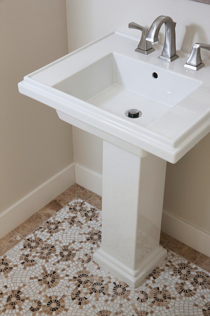 Standwaschbecken mit Armatur auf gemustertem Mosaikfliesenboden in Weiß und Hellbraun