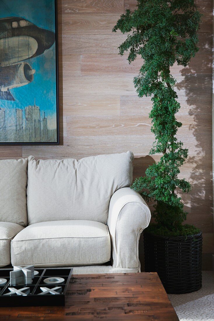 Helle Polstercouch neben Zimmerpflanze vor Wand mit Bild