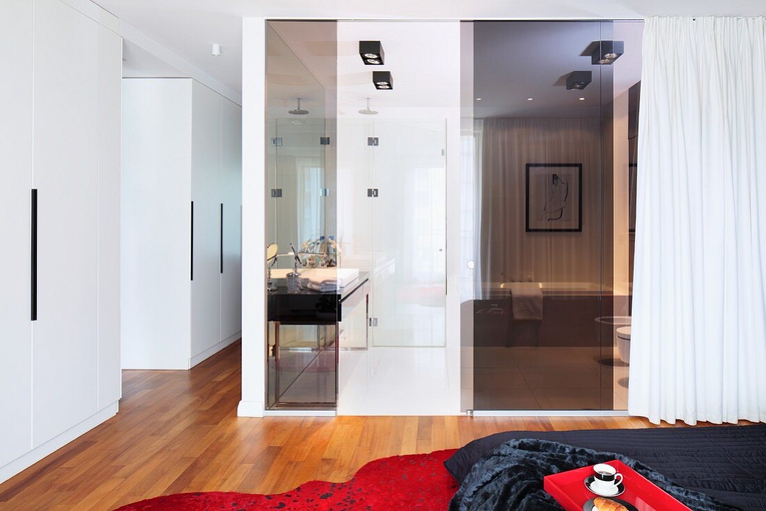 Schlafzimmer mit Bad ensuite, dunkel getönte Glaspaneele vor Badbereich mit weißem Vorhang