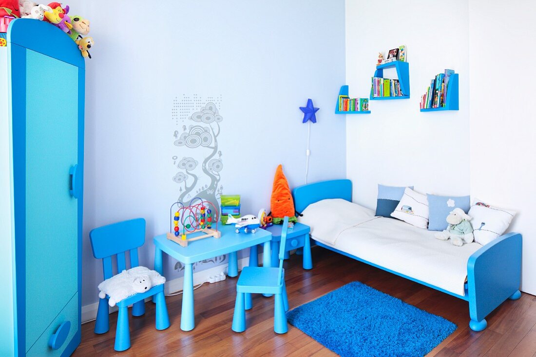 Kinderzimmer in Blau - kleine Stühle um Tisch neben Schlittenbett, an Wand versetzt montierte Konsolen mit Büchern