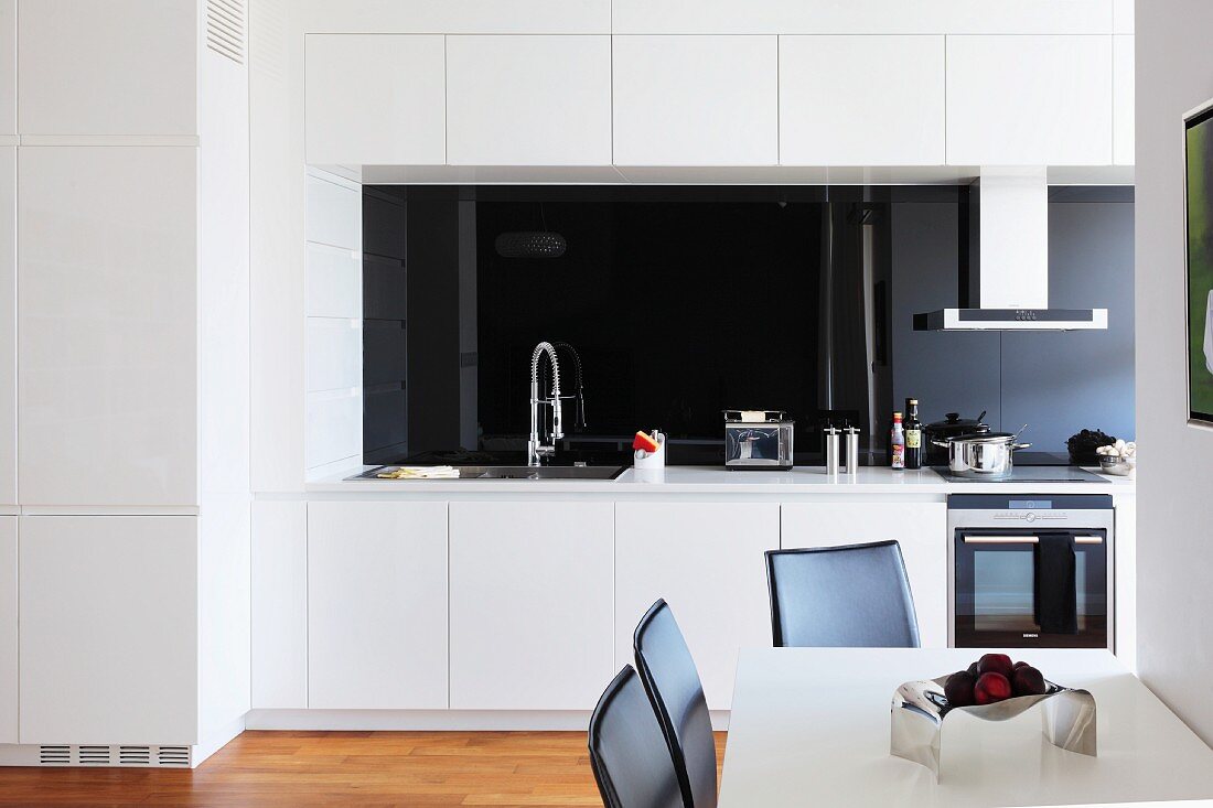 Essplatz in offener, weisser Küche mit schwarzer Glas Rückwand über Arbeitsplatte