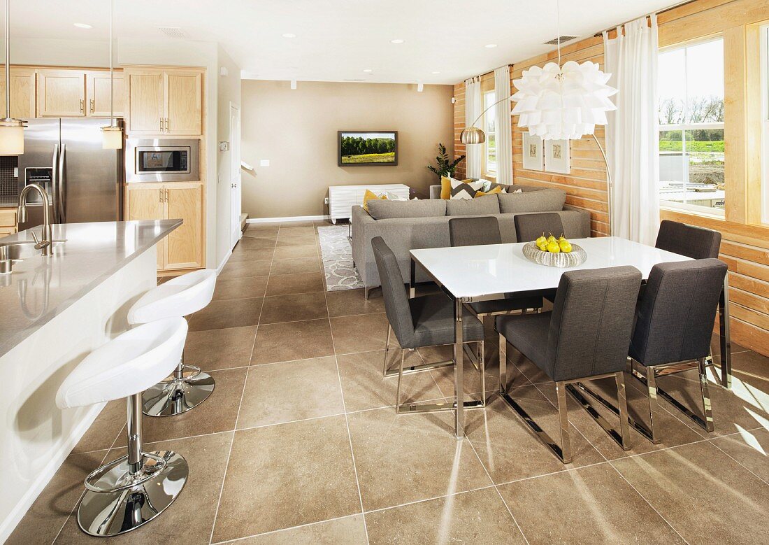 Essplatz mit grauen, gepolsterten Stühlen gegenüber Frühstücks-Bar mit Designer Barhocker, in offenem Wohnhaus mit grauem Fliesenboden