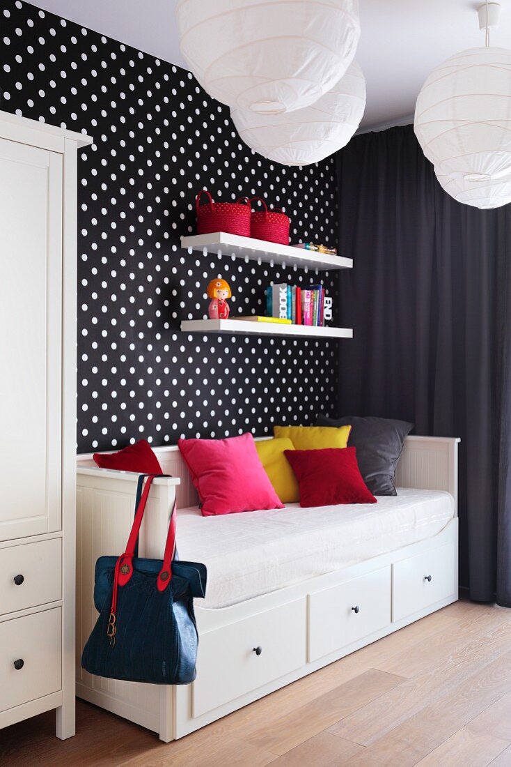 Farbige Kissen auf Schlafsofa mit Schubladen vor schwarzweiss gepunkteter Tapetenwand