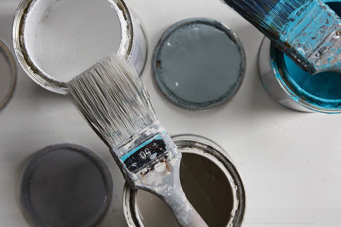 Flat paintbrushes with pale blue and light grey paint residue on open pots of paint