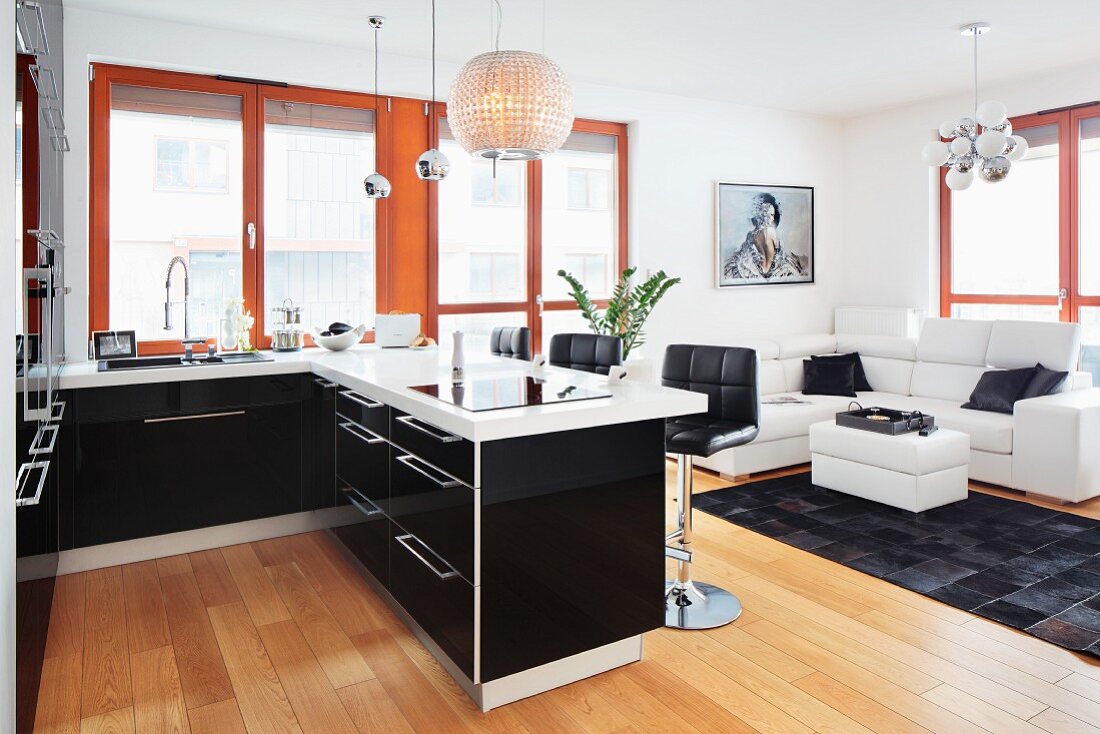 Modern fitted kitchen with a breakfast bar with a view towards a leather sofa in an open, black-and-white living area with designer lamps