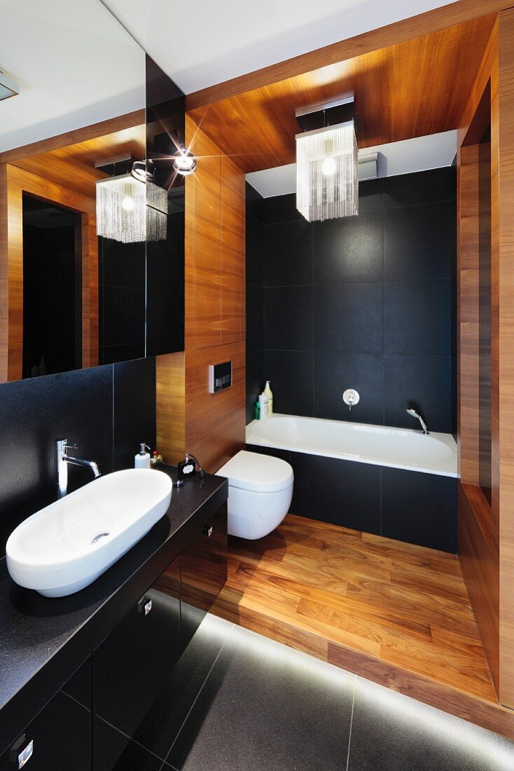 An elegant bathroom with a black and white bathtub and washstand, a wooden panelled toilet section and a modern lamp