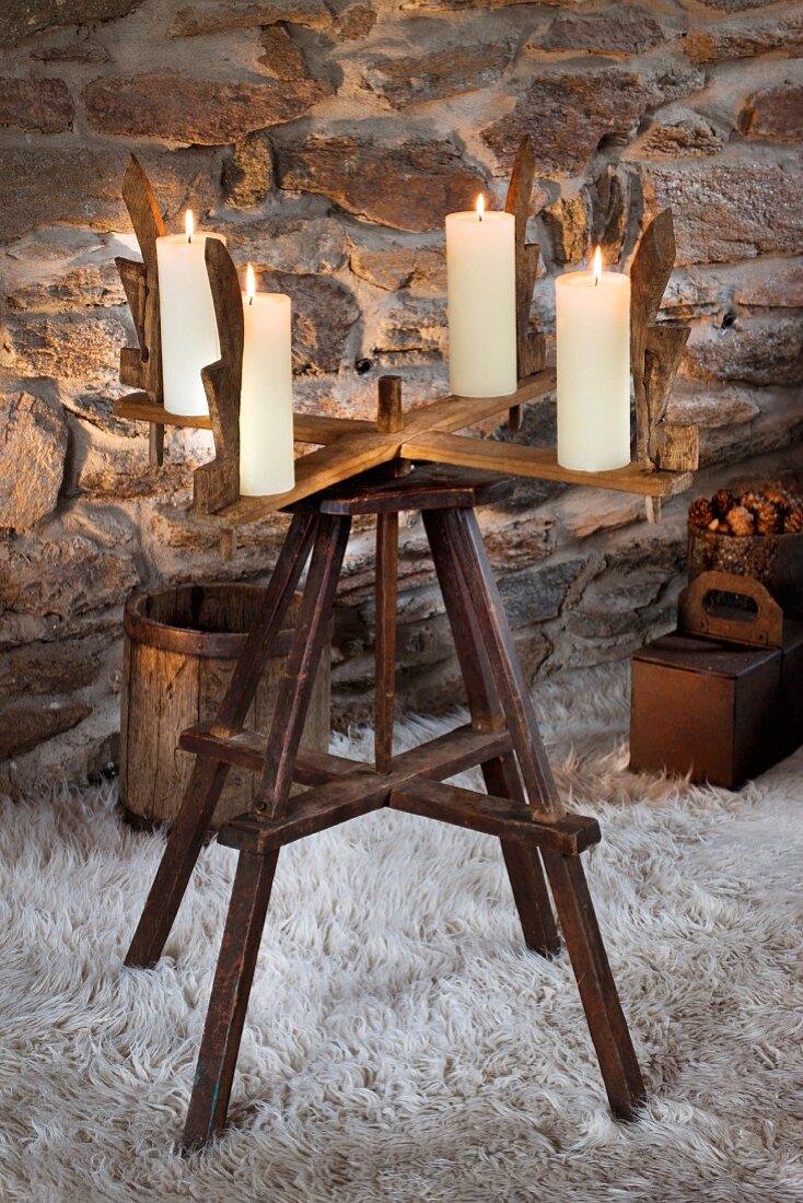 Alte Holzhaspel mit vier Kerzen als Adventskranz auf Flokati vor Naturssteinmauer