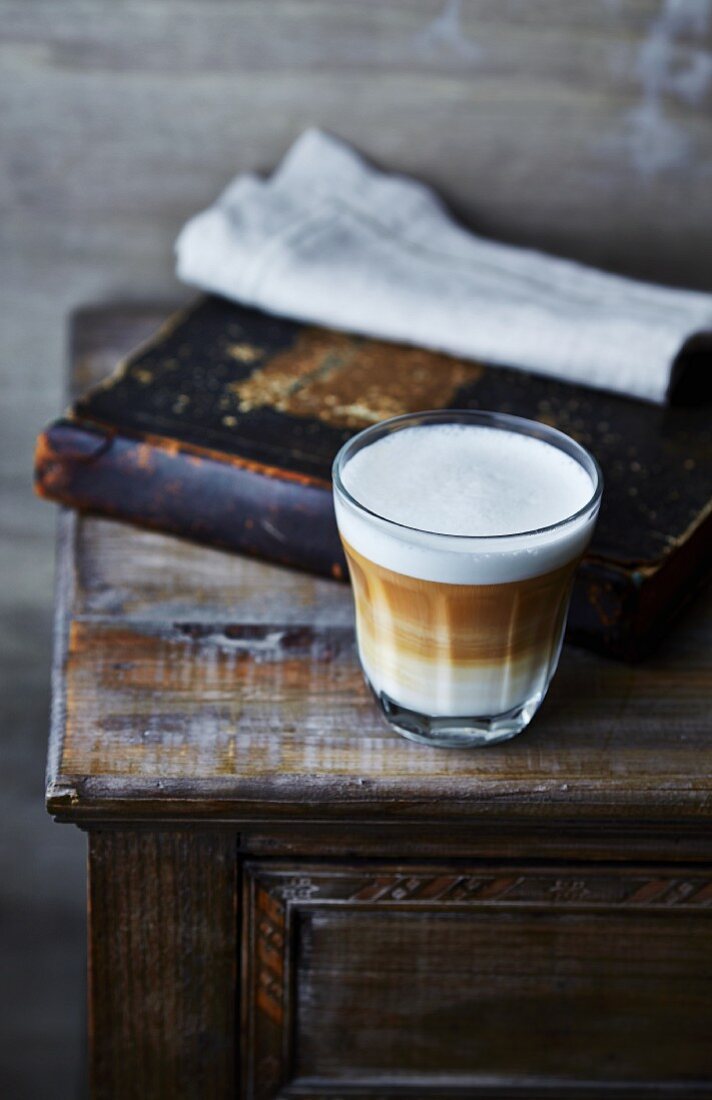 Ein Glas Caffe Latte auf einer alten Kommode