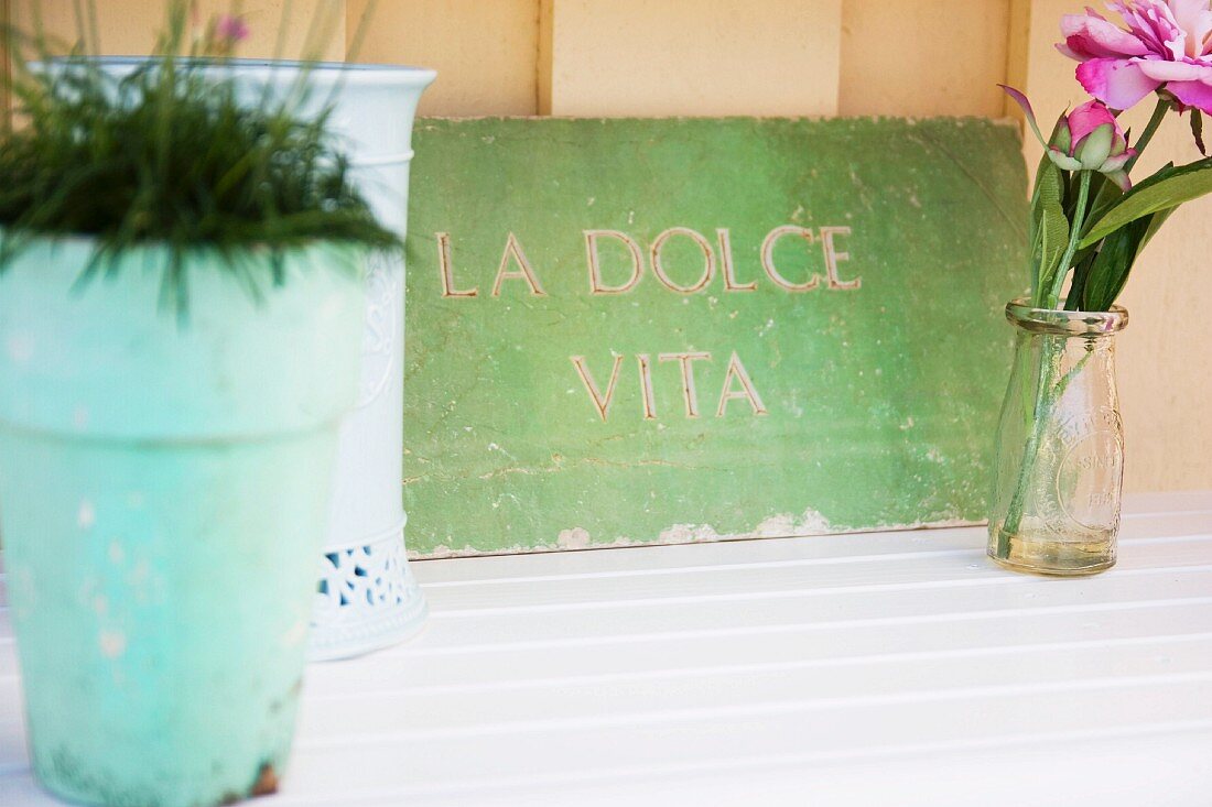 Alte Steinplatte mit gemeisseltem Schriftzug La dolce vita und Pfingstrosenblüte im Glas