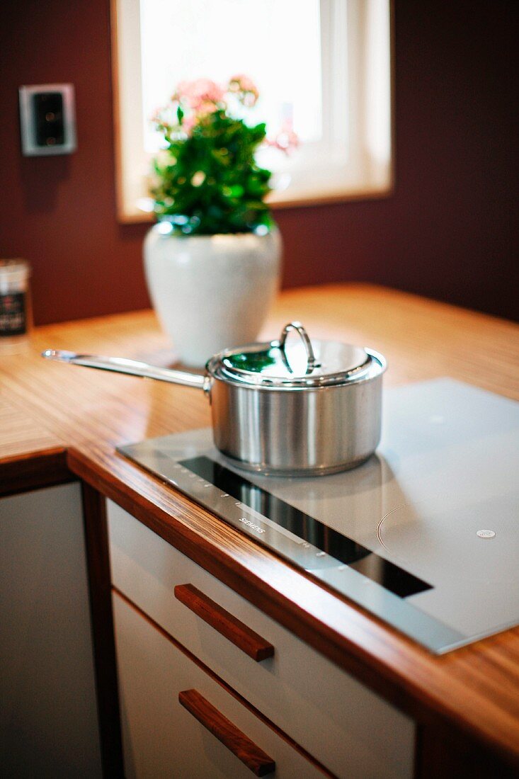 Stainless steel saucepan on hob built into corner worksurface of fitted kitchen
