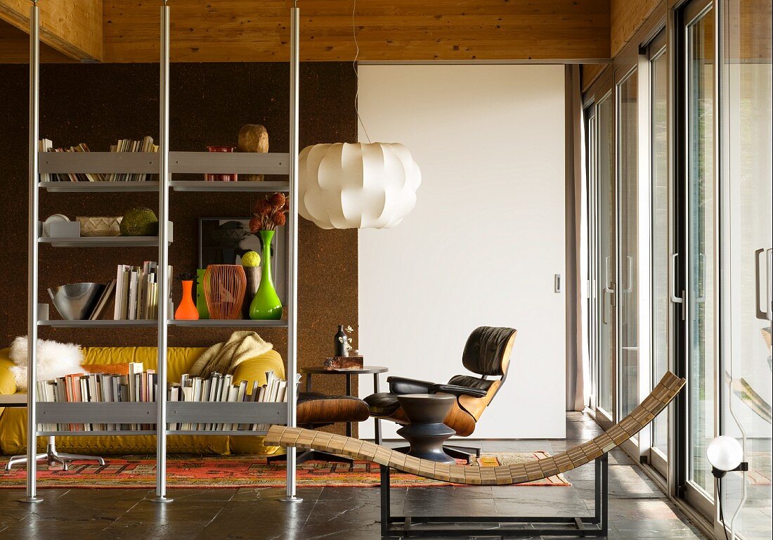 Lässige Liege auf Metallgestell vor Lounge Chair und Edelstahl Regal als Raumteiler vor Wohnbereich