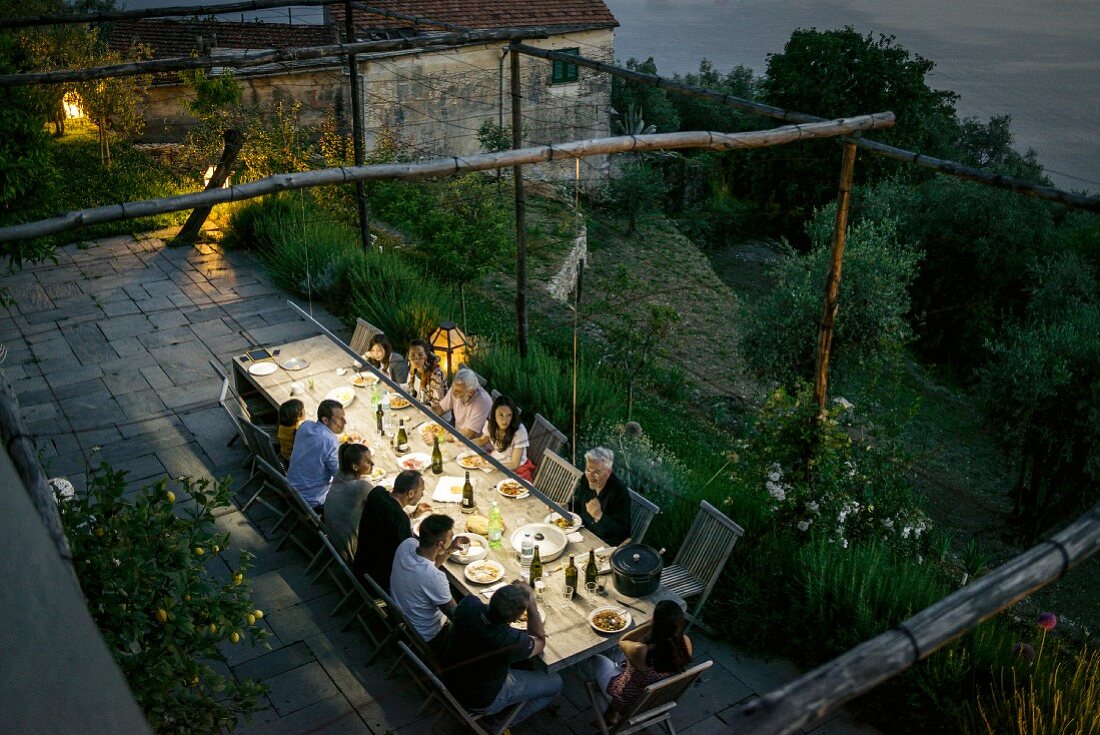 Blick von oben auf die Terrasse eines Rustico im Dämmerlicht mit grosser Runde bei einem italienischen Abendessen