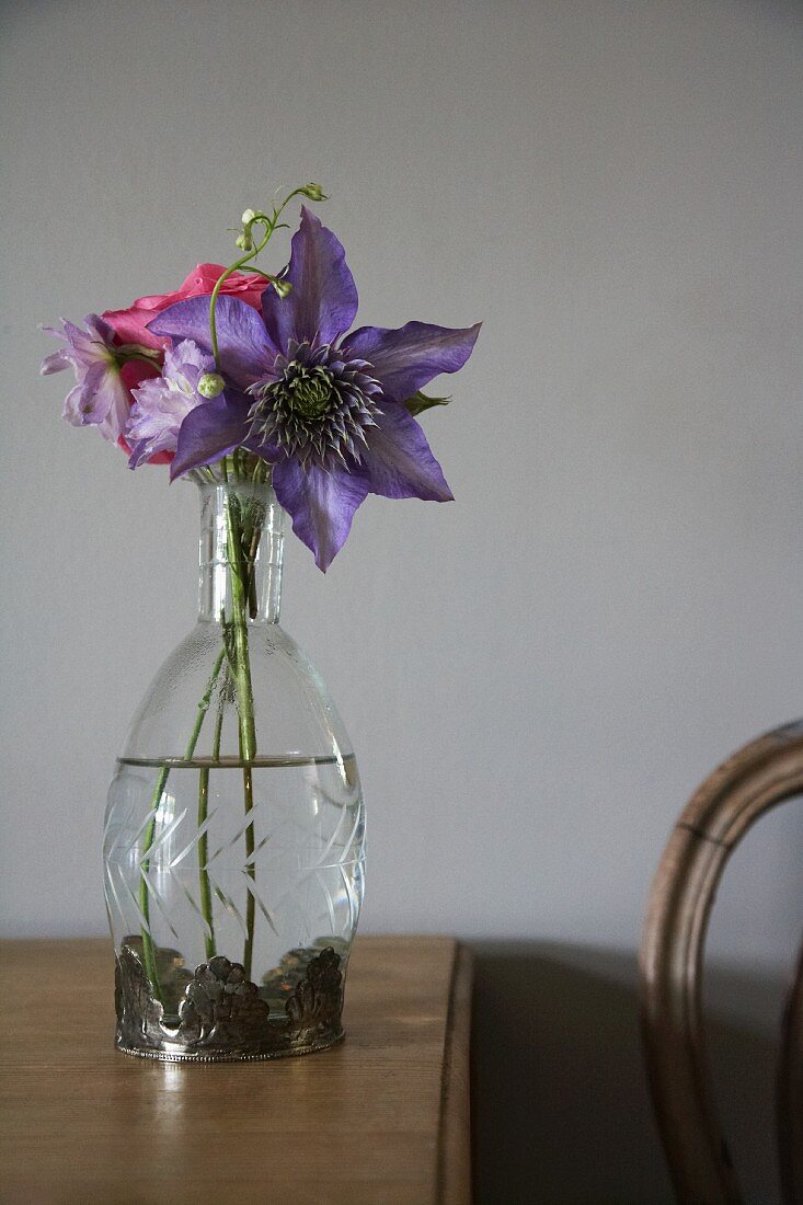 Purple clematis in glass vase on wooden table