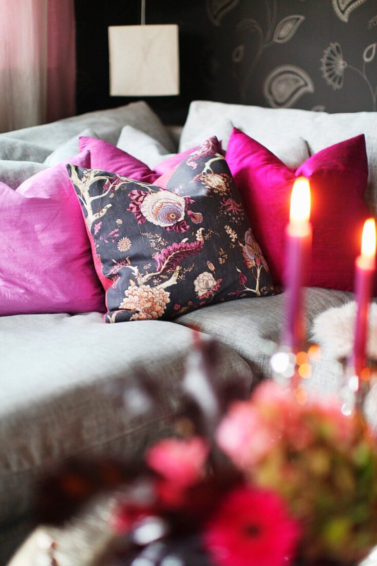 Graues Polstersofa mit pinkfarbenen Kissen und romantischem Kerzenlicht im Vordergrund
