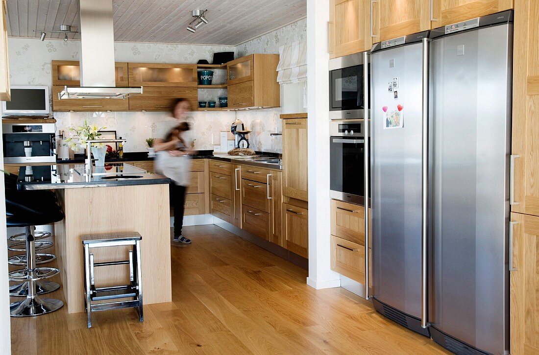 Geräumige offene Küche mit Holzfronten und Parkettboden, an der Küchentheke moderne schwarze Barhocker mit Edelstahlfuß