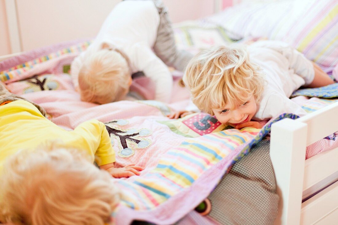 Drei kleine blonde Jungen spielen fröhlich und machen Purzelbäume auf dem Bett