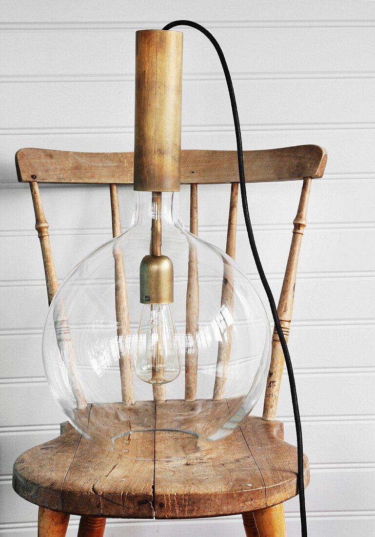 Retropendelleuchte mit Glaslampenschirm auf nostalgischem Holzstuhl vor weißer Holzwand