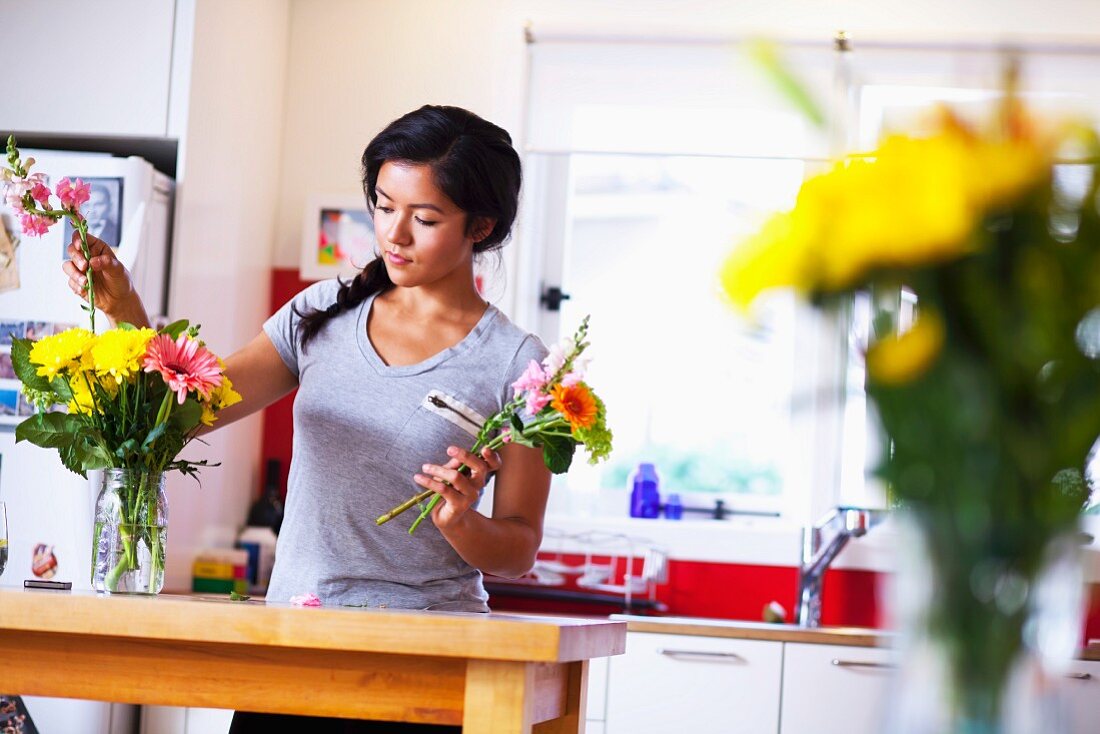 Young woman arranging flowers in kitchen