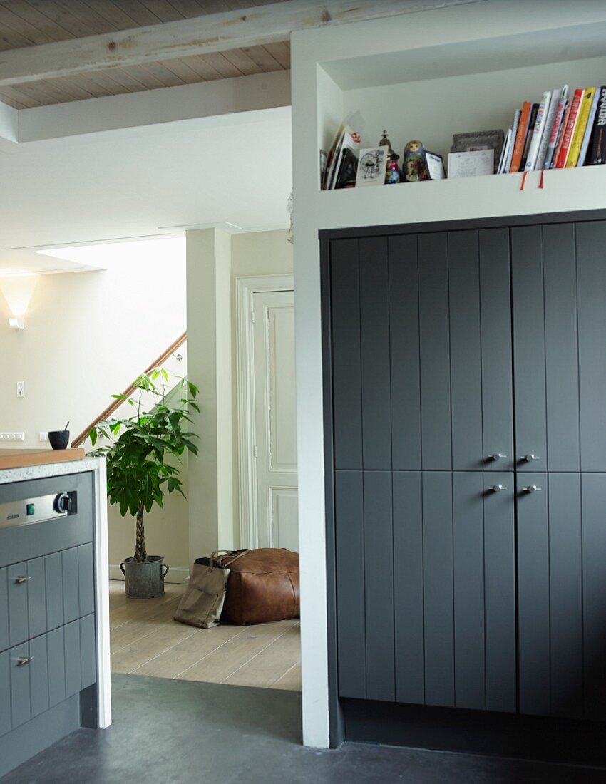 Fitted cupboard with wooden doors painted dark grey below shelf niche and view through open doorway into hall