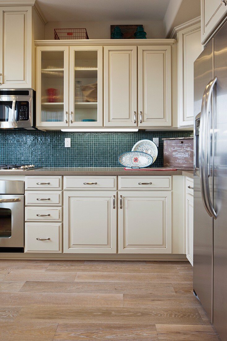 Küche mit weissen Schränken, Elektrogeräten aus Edelstahl & blau gefliester Rückwand