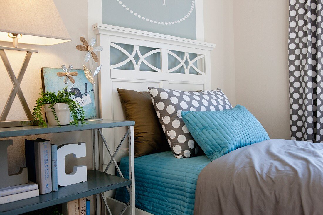Holzbett mit weißem Kopfteil, Bettwäsche & Kissen in Blau und Braun sowie Regal als Nachttisch