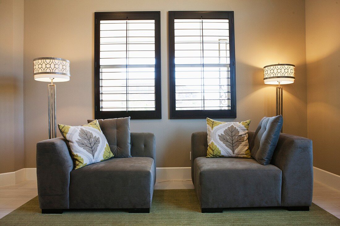 Symmetrisch angeordnete Sitzecke mit grauen Sitzmöbeln & Stehleuchten vor Lamellenfenstern