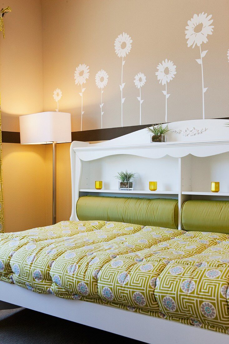 Bett mit Regal im Kopfteil, Stehlampe und aufgemalten Blumenmotiven an Zimmerwand