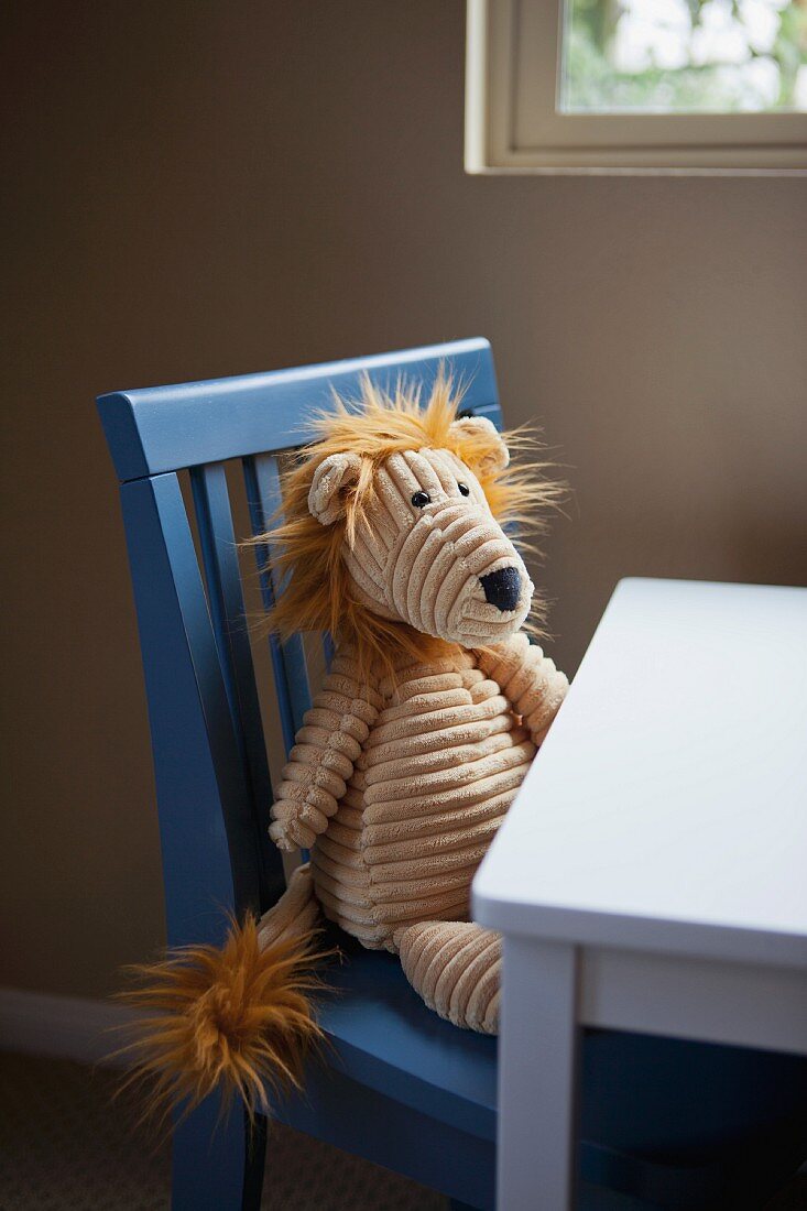 Soft toy sitting on child's chair at table below window
