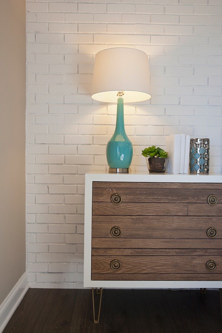 Lit lamp on chest of drawers against wall