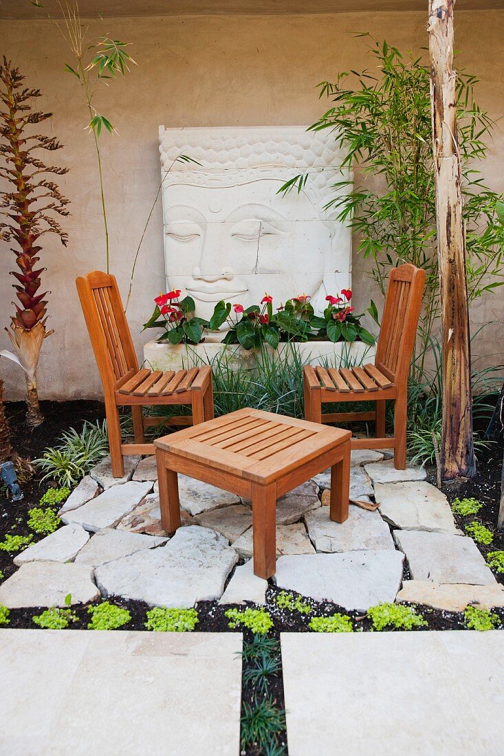 Ruheecke im Garten mit Holzstühlen & Beistelltisch vor Steinplatte mit Buddha-Motiv
